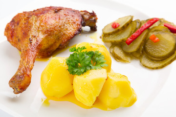 Roast duck leg with potatoes and pickes on the plate