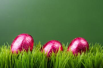 Three red foil Easter eggs on grass