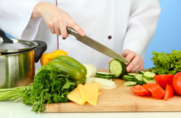 Female hands cutting vegetables, on blue background