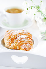 Croissant with coffee, on sunlit breakfast tray