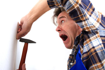 Mann haut sich mit dem Hammer auf den Finger
