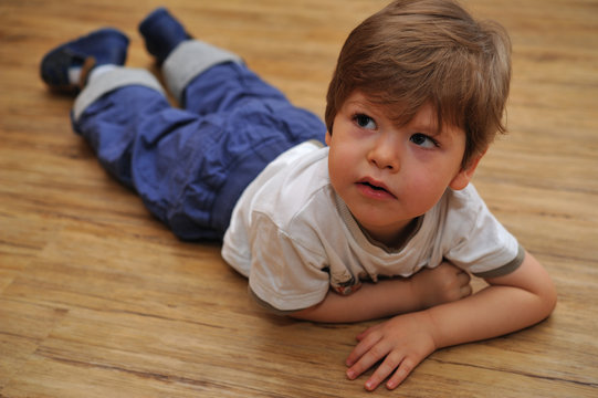 Curious small boy lying on wooden floor