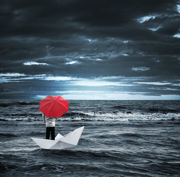 Man with a red umbrella on a paper boat in the stormy sea