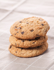 Stacked chocolate chip cookies on brown napkin.
