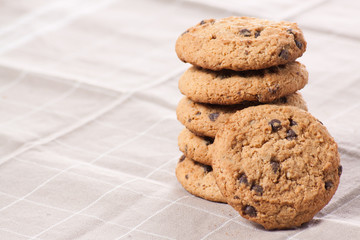 Stacked chocolate chip cookies on brown napkin.