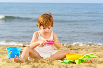 Happy toddler girl playing with her toys at beach