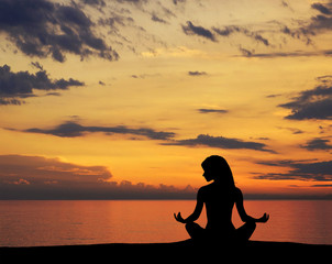 A silhouette of a young woman meditating on a sunset background