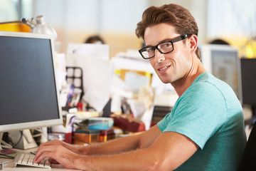 Obraz na płótnie Canvas Man Working At Desk In Busy Creative Office