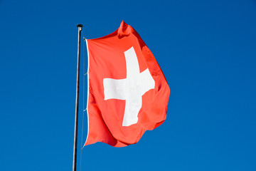 The swiss flag waving in front of a deep blue sky