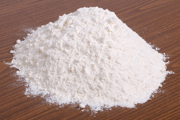 Fototapeta na wymiar Stos białej mąki pszennej na brązowym drewnianym stole