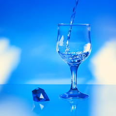 Water pouring into glass on blue background