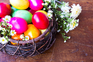 Obraz na płótnie Canvas Colorful easter eggs in brown basket with flower