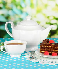 Teapot, cup of tea and delicious cake on natural background