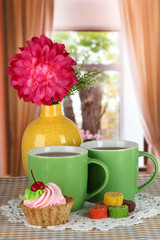 Fototapeta na wymiar Cups of tea with cake,candy and flower on table in room