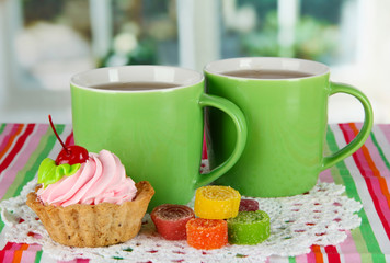 Cups of tea with cake and candy on table in room