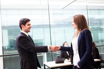 Business handshake at modern office with bussiness people on bac