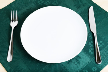 Empty plate, fork and knife on green napkin
