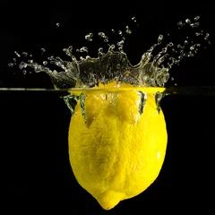 Fotobehang gele citroen valt in het water tegen een zwarte achtergrond © Robert Neumann