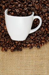 Roasted coffee beans and cup on jute hessian background