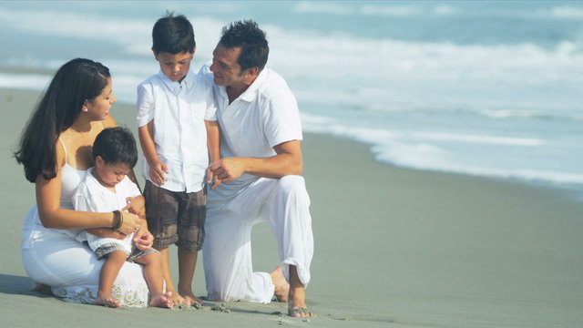 Hispanic family sitting together by ocean dressed in white 