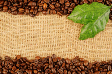 Roasted coffee beans with leaves on jute background