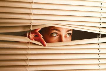 Portrait of a woman looking throughout the blinds