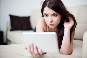 Sad woman lying on couch with tablet