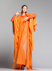 beautiful woman in long orange dress posing in the studio © matusciac