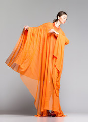 beautiful woman in long orange dress posing in the studio - 50081295