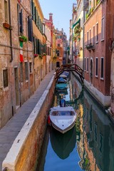 A channel in Venice at the sundown with boats parked around