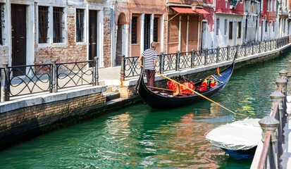 Fototapeta na wymiar Gondolier brodzik jego gondola przez mały kanał w Wenecji