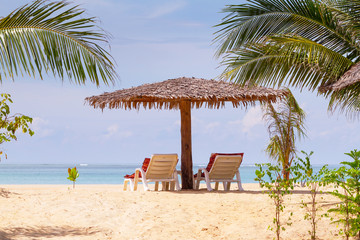 Tropical beach scenery with parasol and deck chairs in Thailand