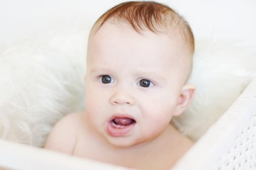 Dissatisfied baby sits in white basket