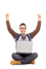 Happy male student sitting with a laptop and gesturing happiness