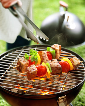 Person turning kebabs on a barbecue