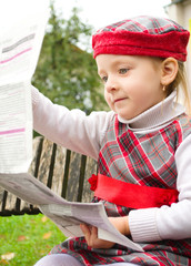 Little girl is reading a newspaper