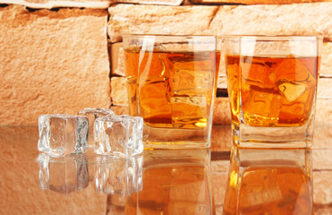 Glasses of whiskey and ice on brick wall background