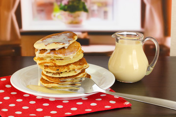 Sweet pancakes on plate with condensed milk on table in room