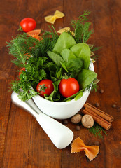Herbs and spices in ceramic mortar, on wooden background