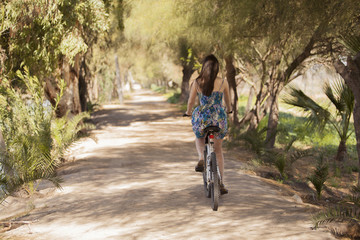 Fototapeta premium Young woman riding her bicycle away and surrounded by trees