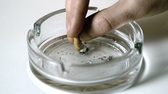 Hand extinguishing cigarette in empty ashtray