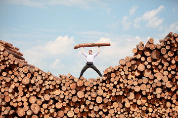 man on  top of large pile of logs, shouting, lifting heavy log
