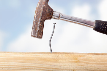 Crooked nail in the wooden board with a hammer