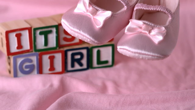 Baby shoes falling on pink blanket with its a girl in blocks