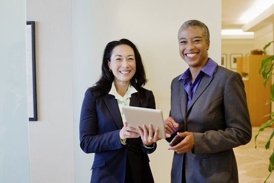 Businesswomen using digital tablet in office corridor
