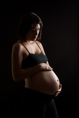 Pregnant Peruvian woman touching her belly against black backgro