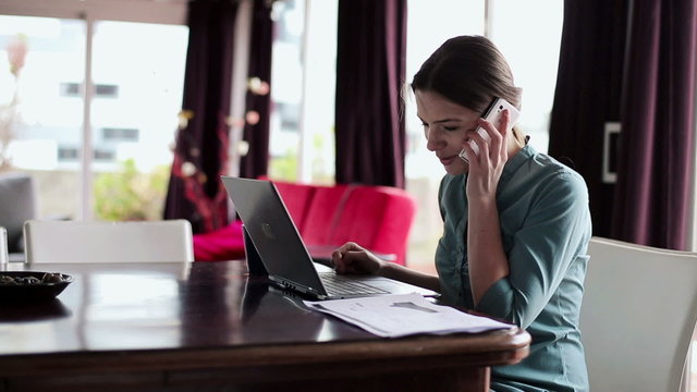 Young businesswoman working with cellphone and laptop in home