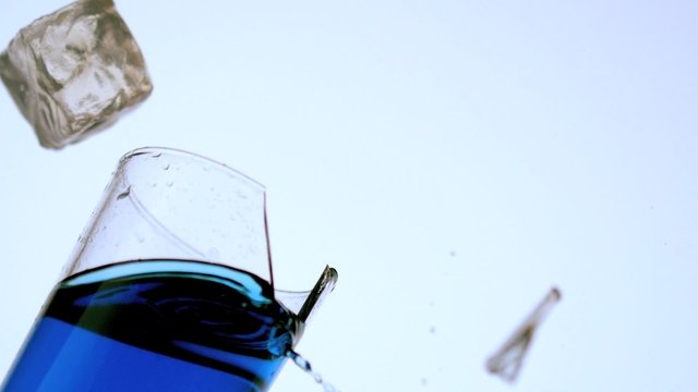 Ice falling and breaking glass of blue liquid