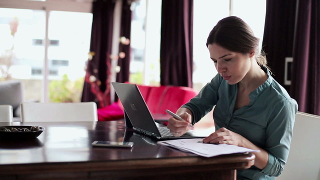 Young businesswoman working with documents and laptop in home