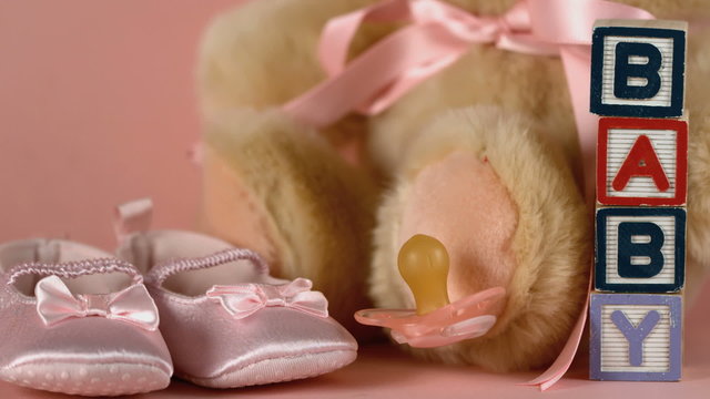 Pink soother falling besides baby shoes blocks and teddy bear